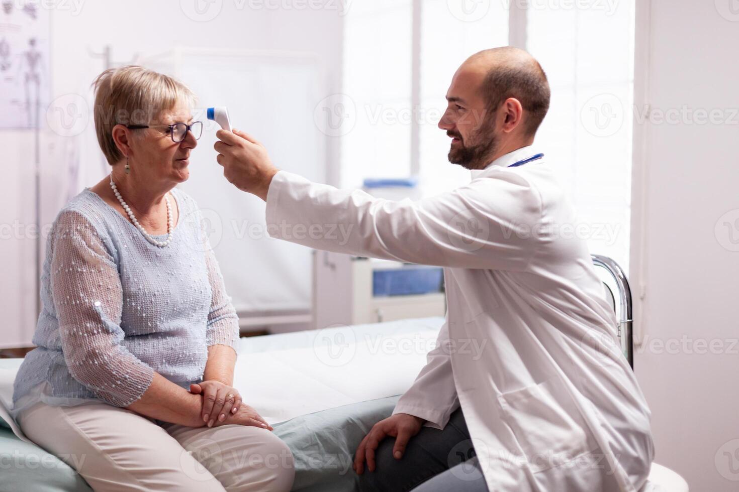 Measuring old senior woman temperature during consultation in clinic examination room. Medical consultation for infections and disease during global pandemic,flu, tool, sickness. photo