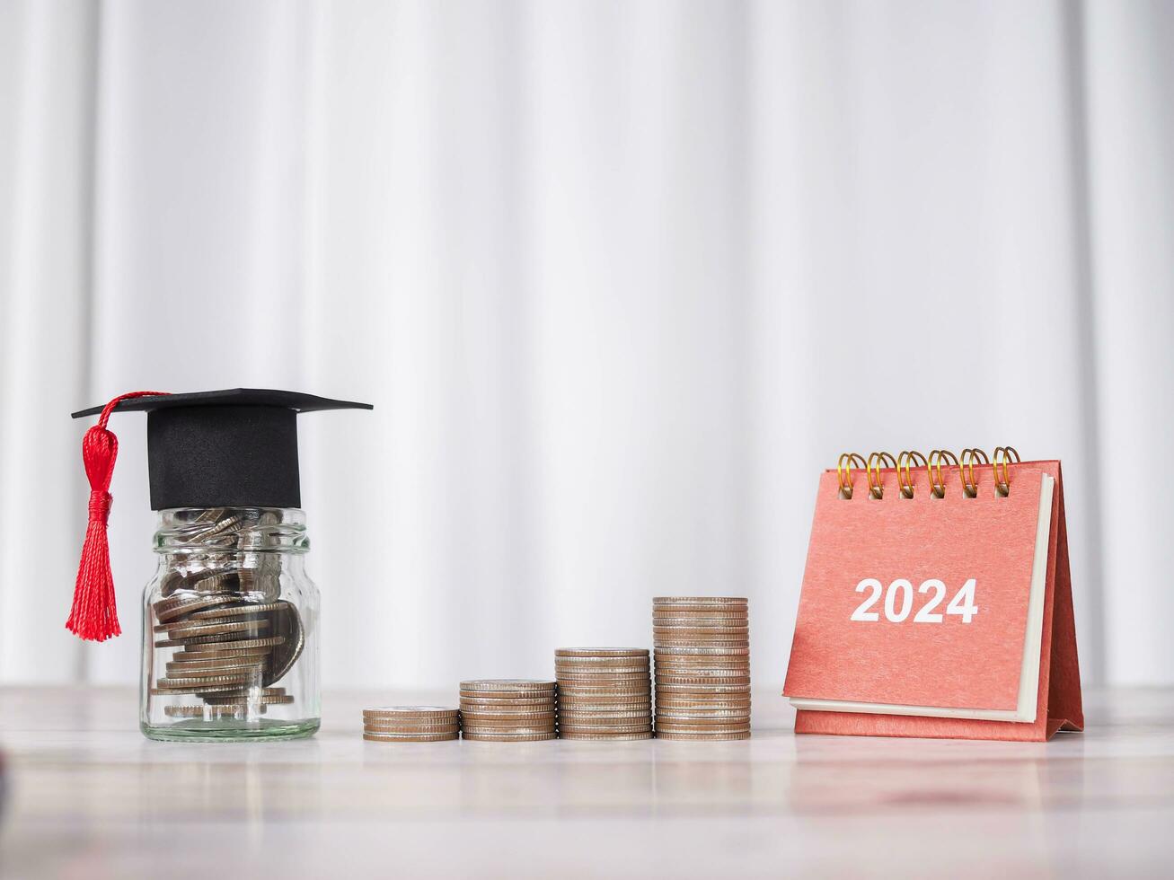 2024 desk calendar, Glass bottle with graduation hat and stack of coins. The concept of saving money for education, student loan, scholarship, tuition fees in Year 2024 photo