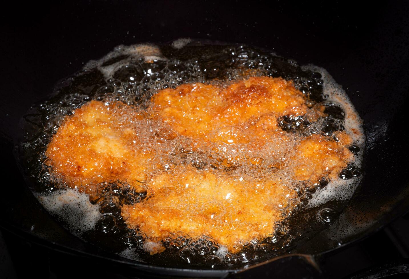 empanizado frito pollo. comidas frito en hirviendo petróleo en un chino wok Cocinando por fritura en caliente aceite. burbujas Aparecer desde fritura foto