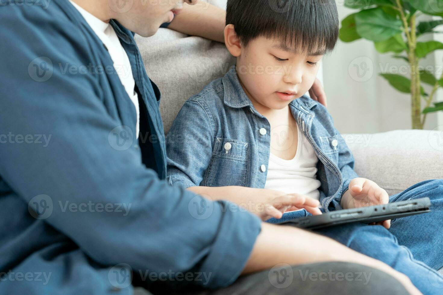 Happy single father playing teach using tablet with the little boy. family is happy and excited in the house. Father and son having spending time together, Good daddy , addiction fix, handle, control photo