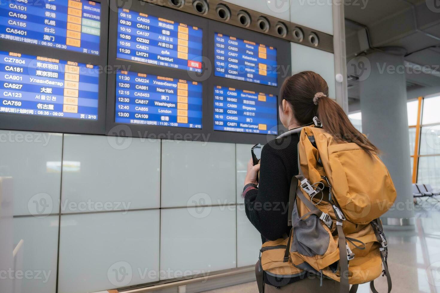 Young Asian woman in international airport looking at flight information board, checking her flight photo