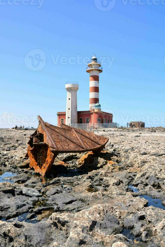 an old boat is sitting on the rocks near a lighthouse photo