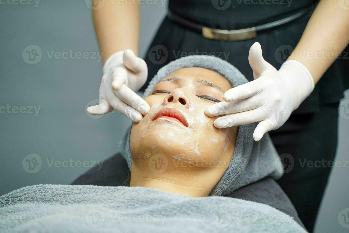 Closeup cosmetologist applying smooth facial white mask cream and massage on beauty woman making face spa in beauty clinic. photo