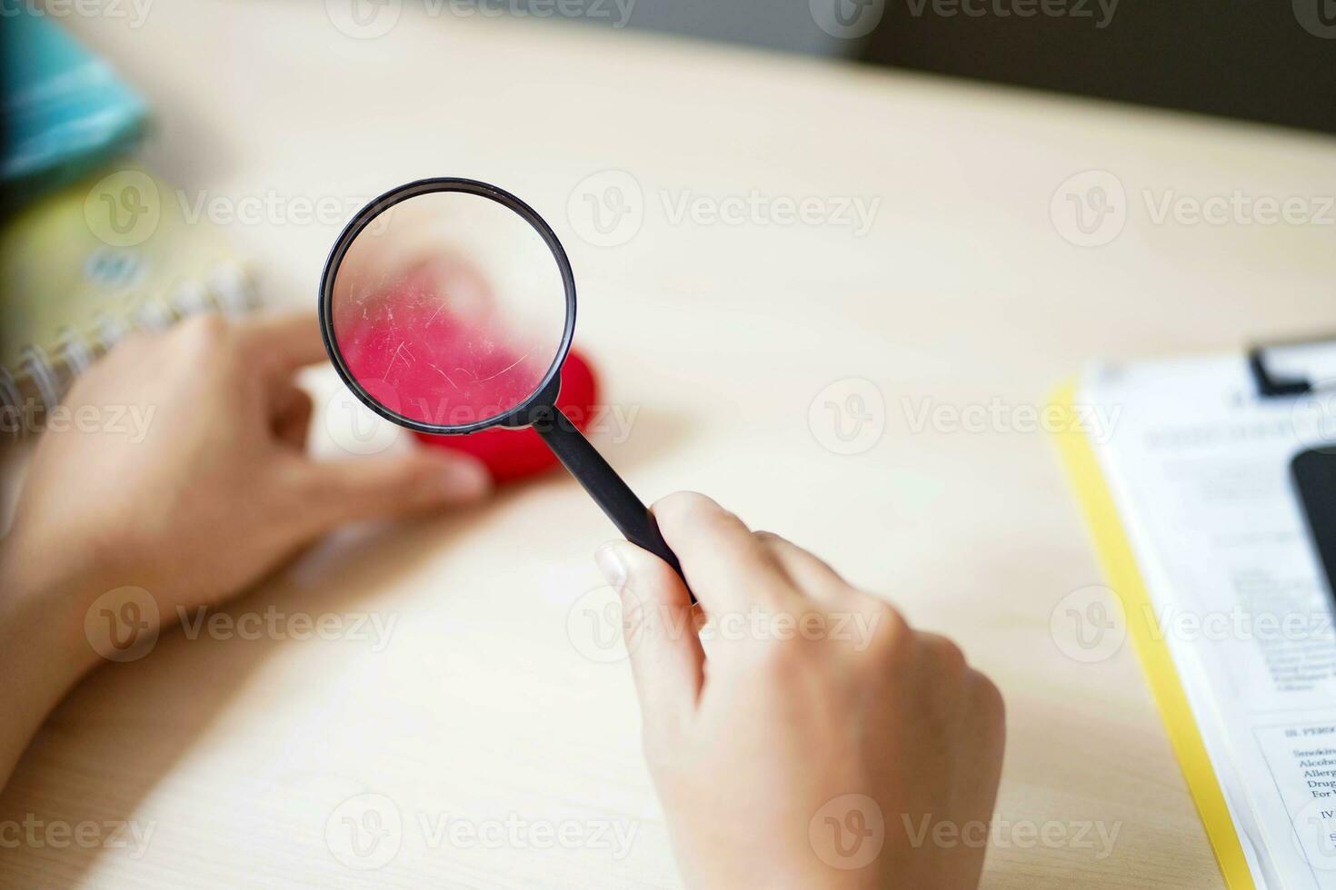 Closeup hands of medical student holding a magnifying glass on a yarn red heart and blurred background. Asian medical student with Heart disease concept. photo