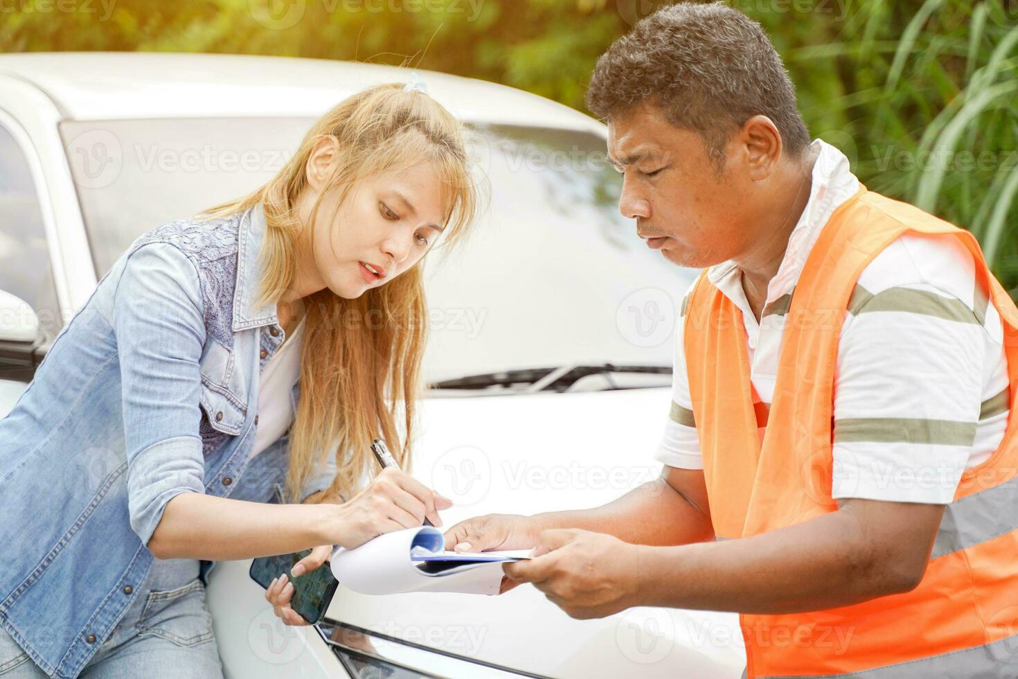The insurance agent inspects the damaged vehicle and The customer signs the filing of the post-accident claim report form. Traffic accident and insurance concept photo