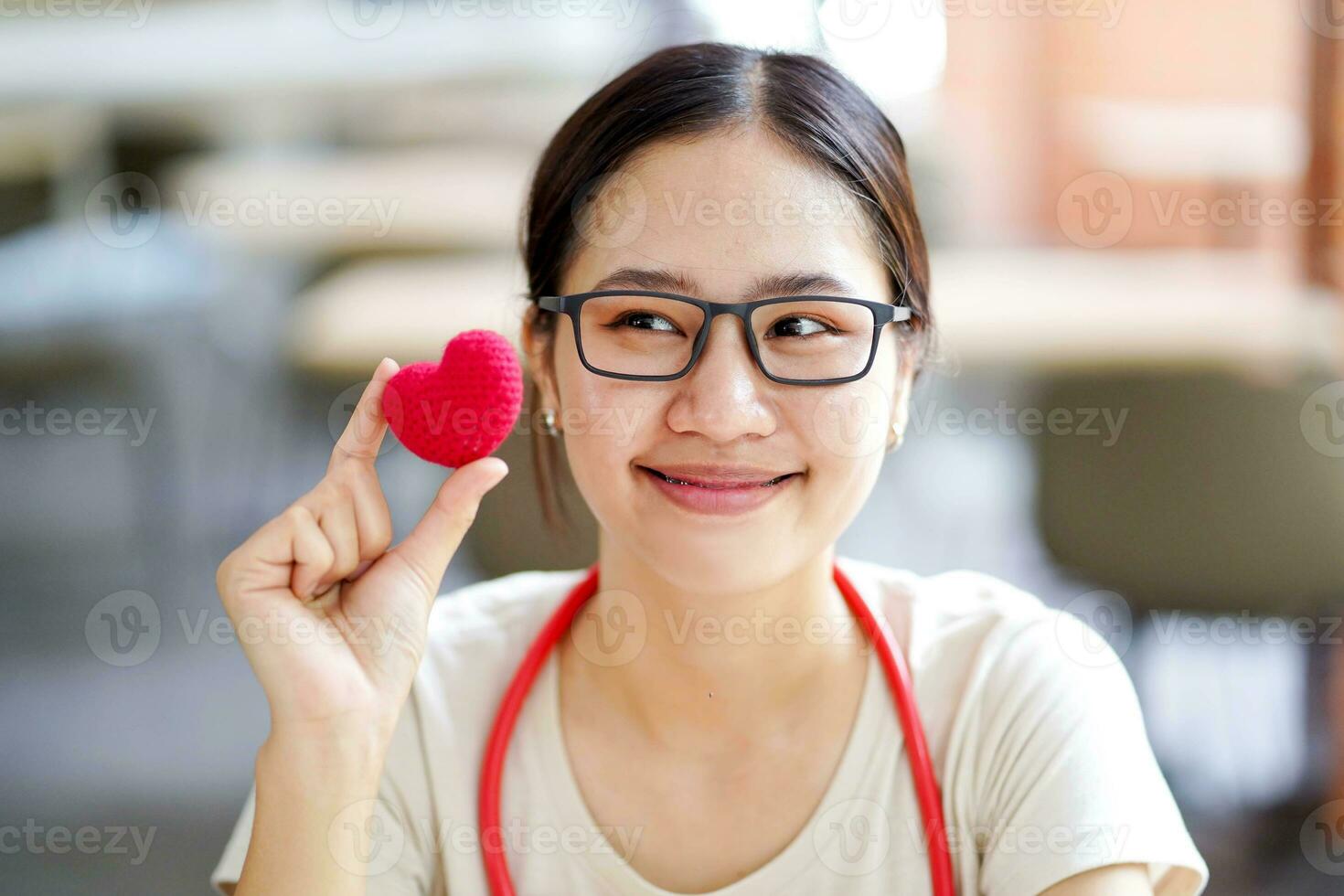 Closeup medical student action holding a rubber red heart with cute smile on blurred background. Asian medical student with Heart disease concept. photo