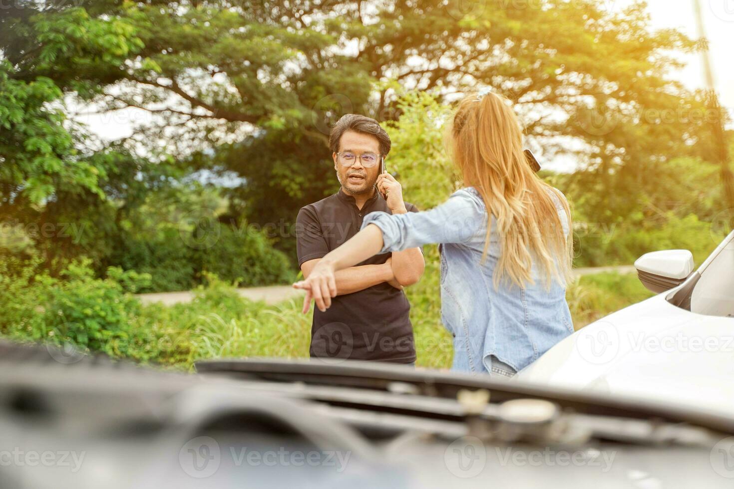 Drivers stood arguing and call to insurance company after the car crashed on country road with sun flare background. photo