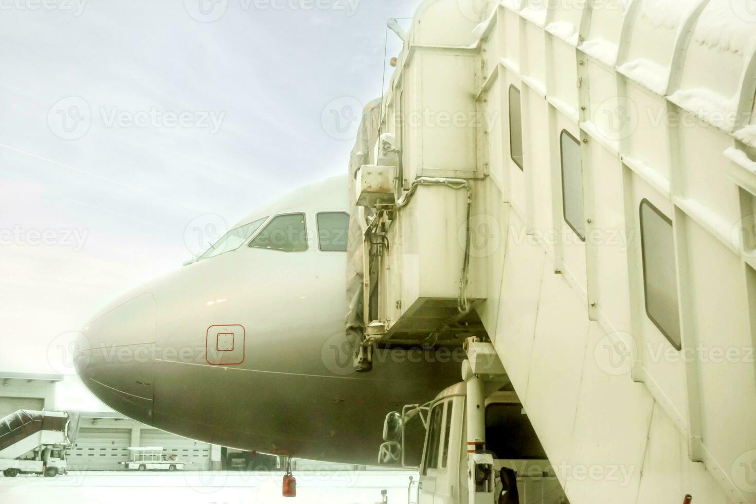 Closeup jet bridge and white airplane parked on airport ground and winter blue sky background. photo