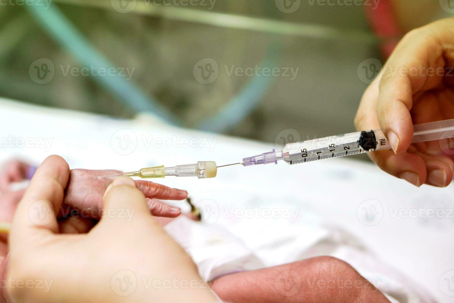 Nurse hands gradually stab injecting medicine from syringe pass IV Catheter at sick newborn baby's hands. photo