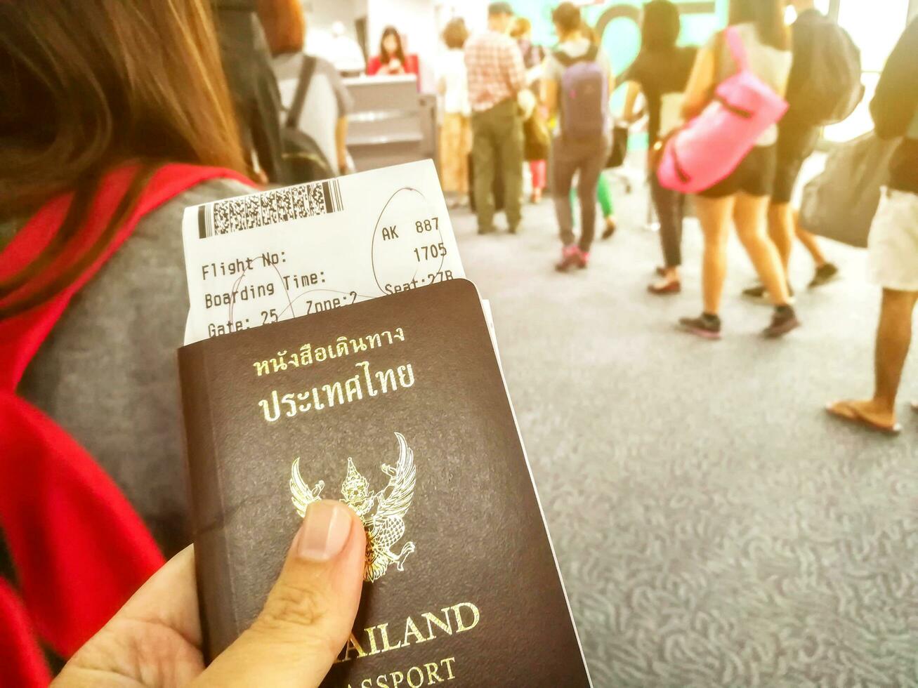 Bangkok City, 2018 -Hand of Thai citizen holding the Thailand passport with airplane boarding pass and line up to check in airline counter on blurry many tourists and sun flare in airport. photo