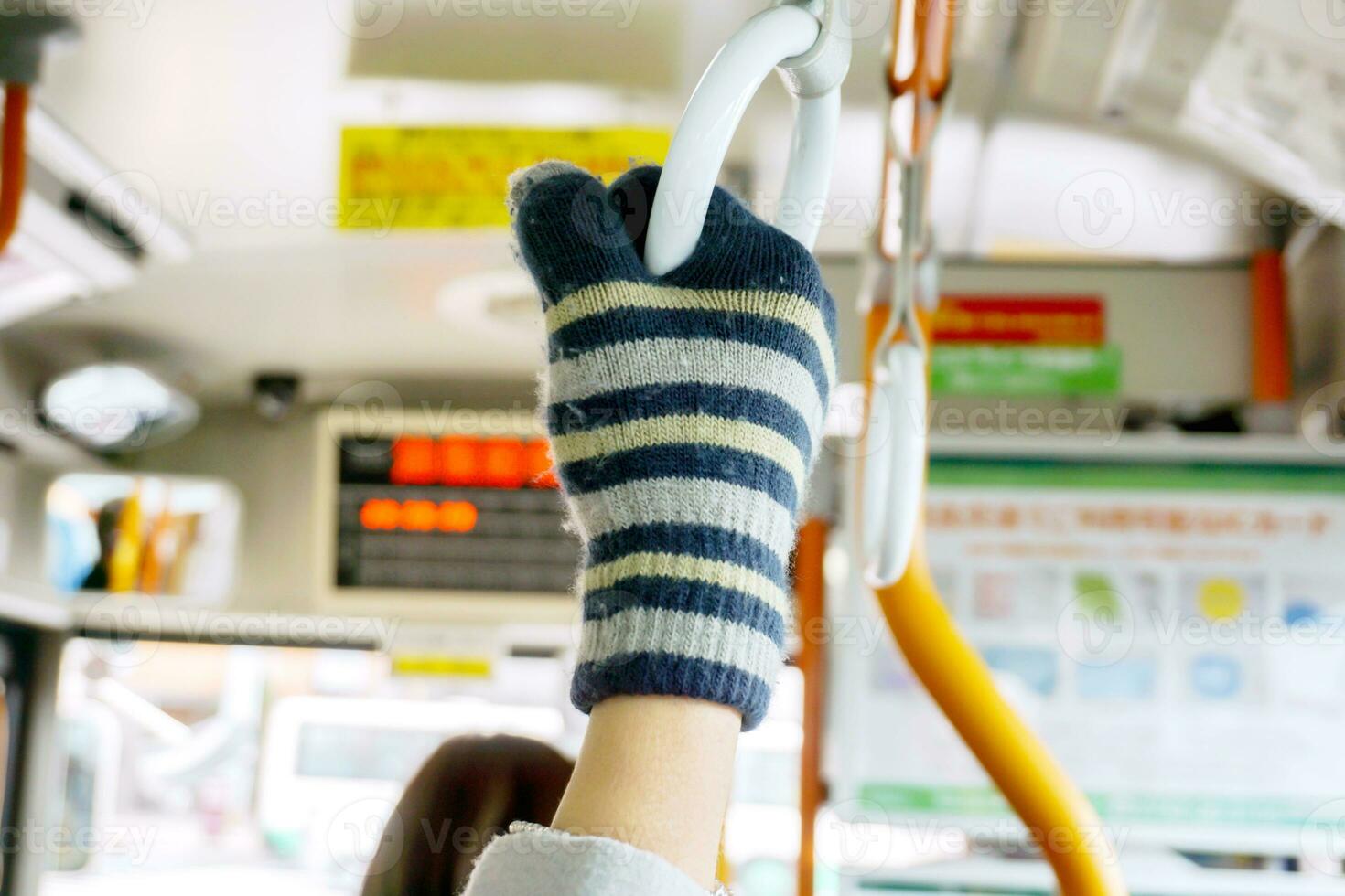 Hand in yarn glove holding handle loop in a loop bus on blurry background. photo