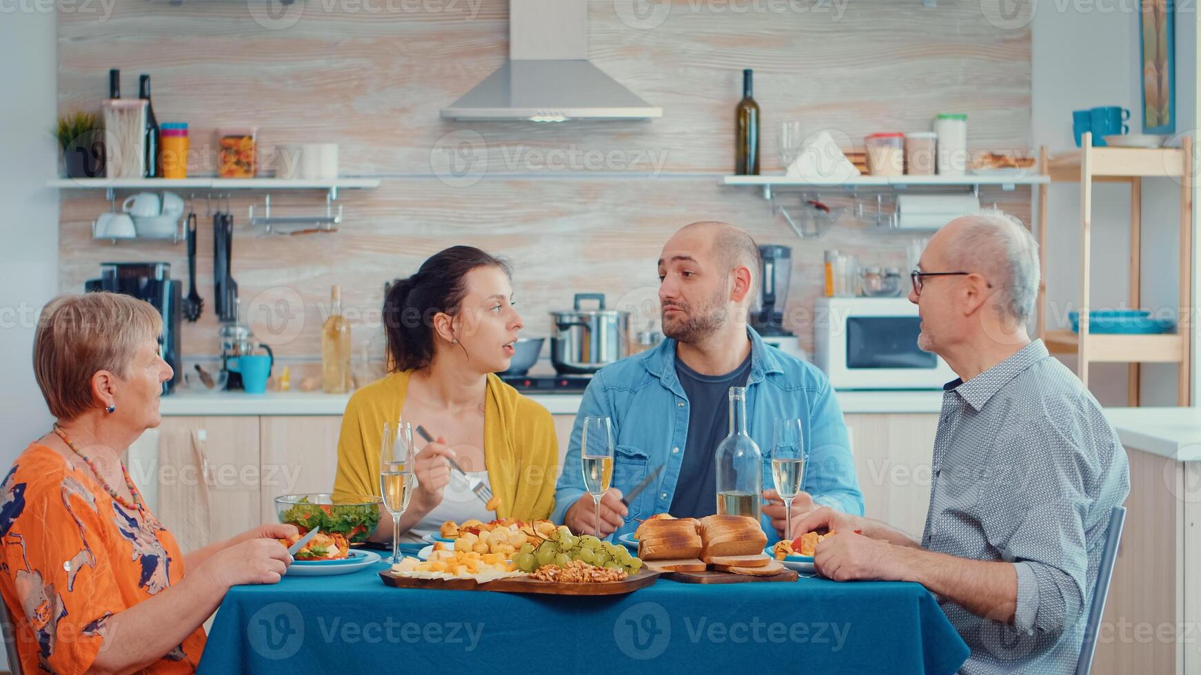 extendido familia hablando teniendo relajante tiempo. multi Generacion disfrutando hora a hogar, en el cocina sentado por el mesa, comiendo cena juntos y Bebiendo foto