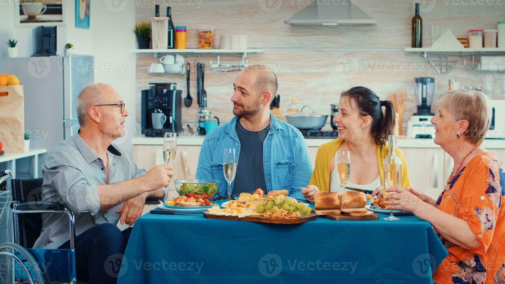 Elderly man with disability having good news for his family. Older senior in wheelchair smiling, drinking wine and eating during a gourmet meal, enjoying relaxing time. photo