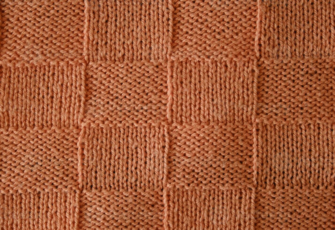 Texture of smooth knitted sweater with pattern. Handmade knitting wool or cotton fabric texture. Unusual abstract knitted chess pattern background texture. Peach Fuzz colour of 2024 year photo