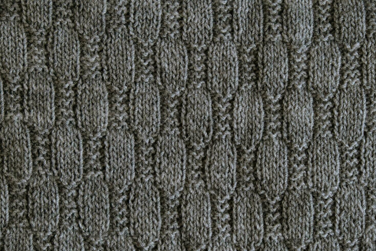 Texture of smooth knitted gray sweater with pattern. Top view, close-up. Handmade knitting wool or cotton fabric texture. Background with knitted leaf shape, knitting pattern with cables. photo