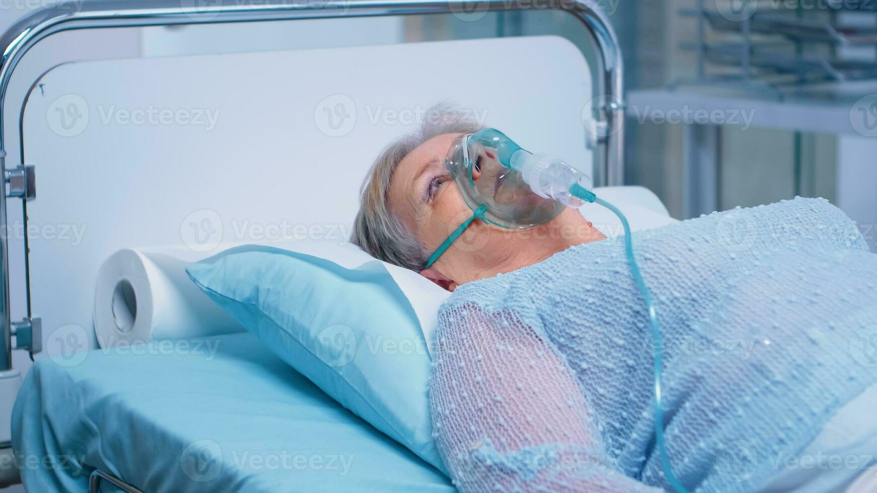 Retired senior old woman breathing with oxygen mask, lying in hospital bed getting treatment for infection. Coronavirus covid-19 medical medicine pandemic healthcare system photo