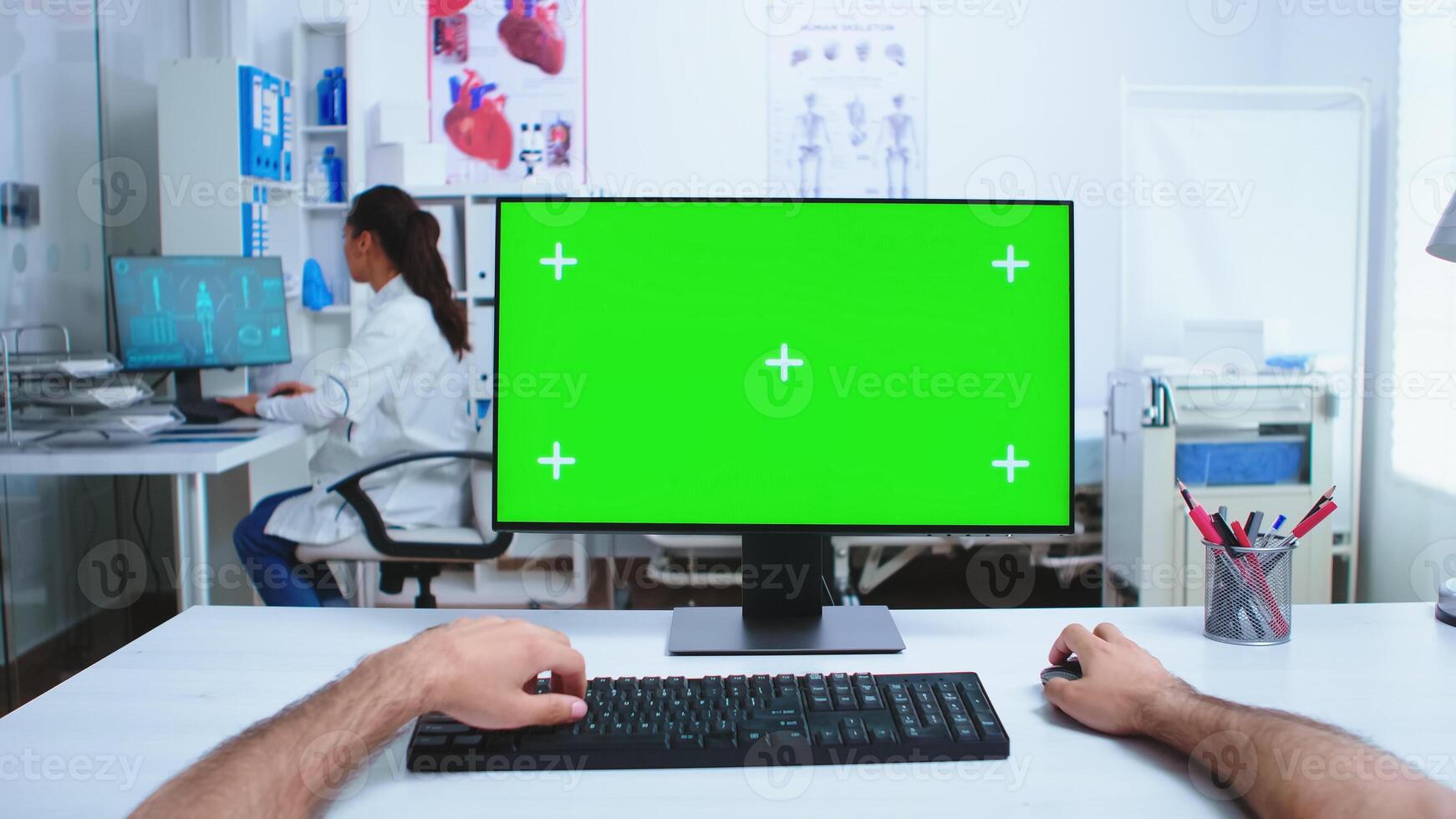 Pov of medical practitioner using computer with copy space available in hospital cabinet and doctor in the background. Medical physician in clinic cabinet working desktop with green screen available. photo