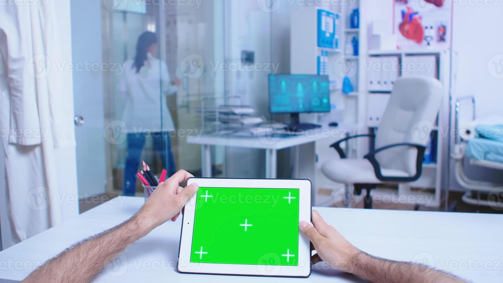Pov shot of medic tapping on tablet pc with green screen in hospital cabinet. Doctor leaving from private clinic wearing white coat. Medic using tablet with chroma key on display in medical clinic. photo