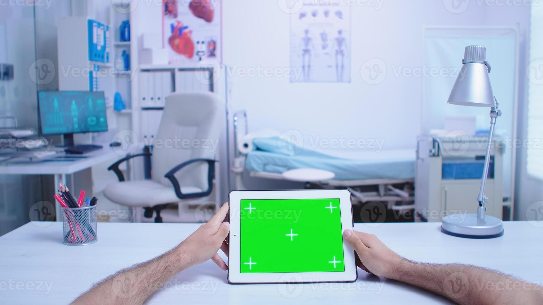 pov Disparo de asistente participación tableta ordenador personal con verde pantalla en hospital gabinete y médico vistiendo blanco Saco trabajando en computadora. médico utilizando tableta con croma llave en monitor en médico clínica. foto