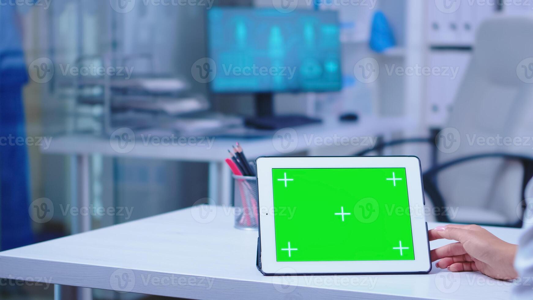 Close up of doctor using tablet computer with green chroma key in hospital cabinet. Doctor in health clinic working on tablet computer with replaceable screen doing medicine research. photo