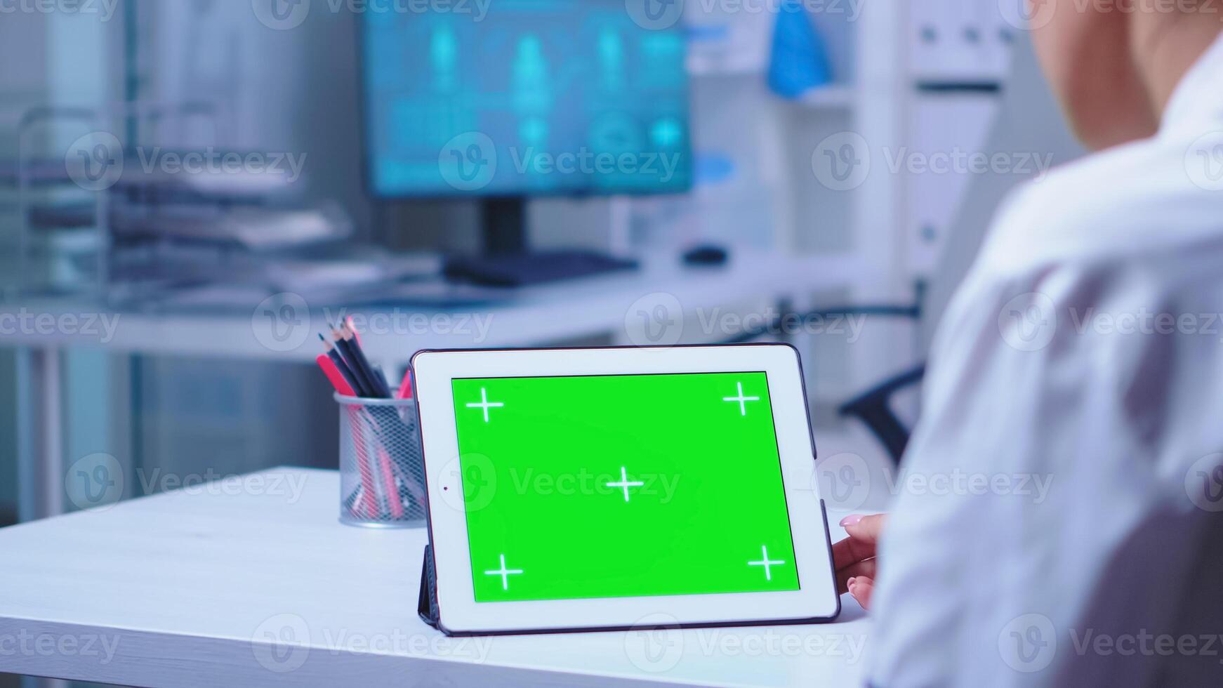 tableta ordenador personal con verde pantalla en hospital gabinete usado por médico vistiendo blanco abrigo. enfermero en azul uniforme entrando en clínica. médico en salud clínica trabajando en tableta computadora con reemplazable pantalla haciendo medicina investigación. foto