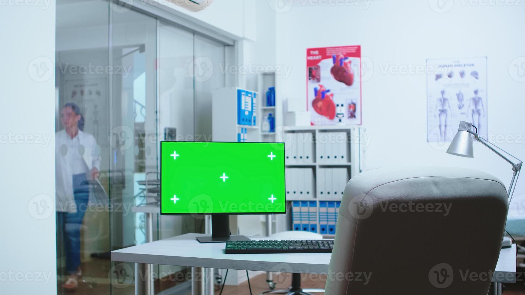 Computer with mock-up display in hospital cabinet and doctor entering in clinic. Desktop with blank and copy space green screen isolated available on display of medicine specialist in clinic cabinet. photo