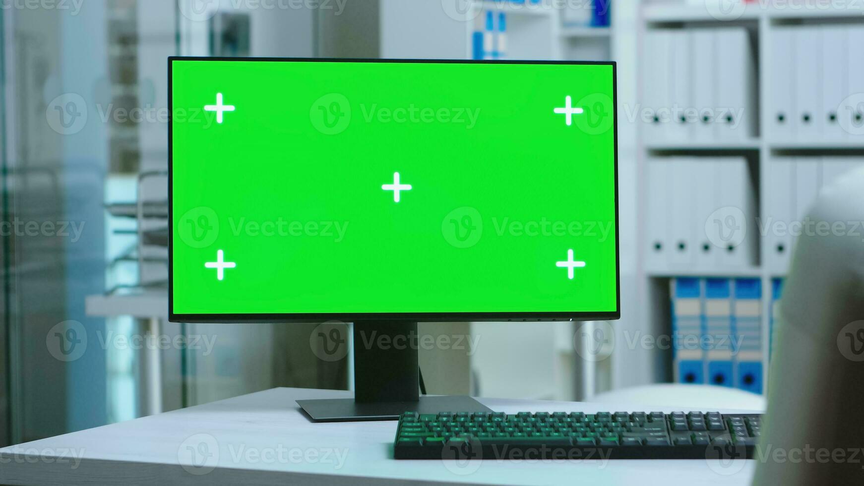 Dolly shot of computer with green screen in private hospital and personnel wearing uniform in the background. PC with blank and copy space green screen available on display of medicine specialist in clinic cabinet. photo