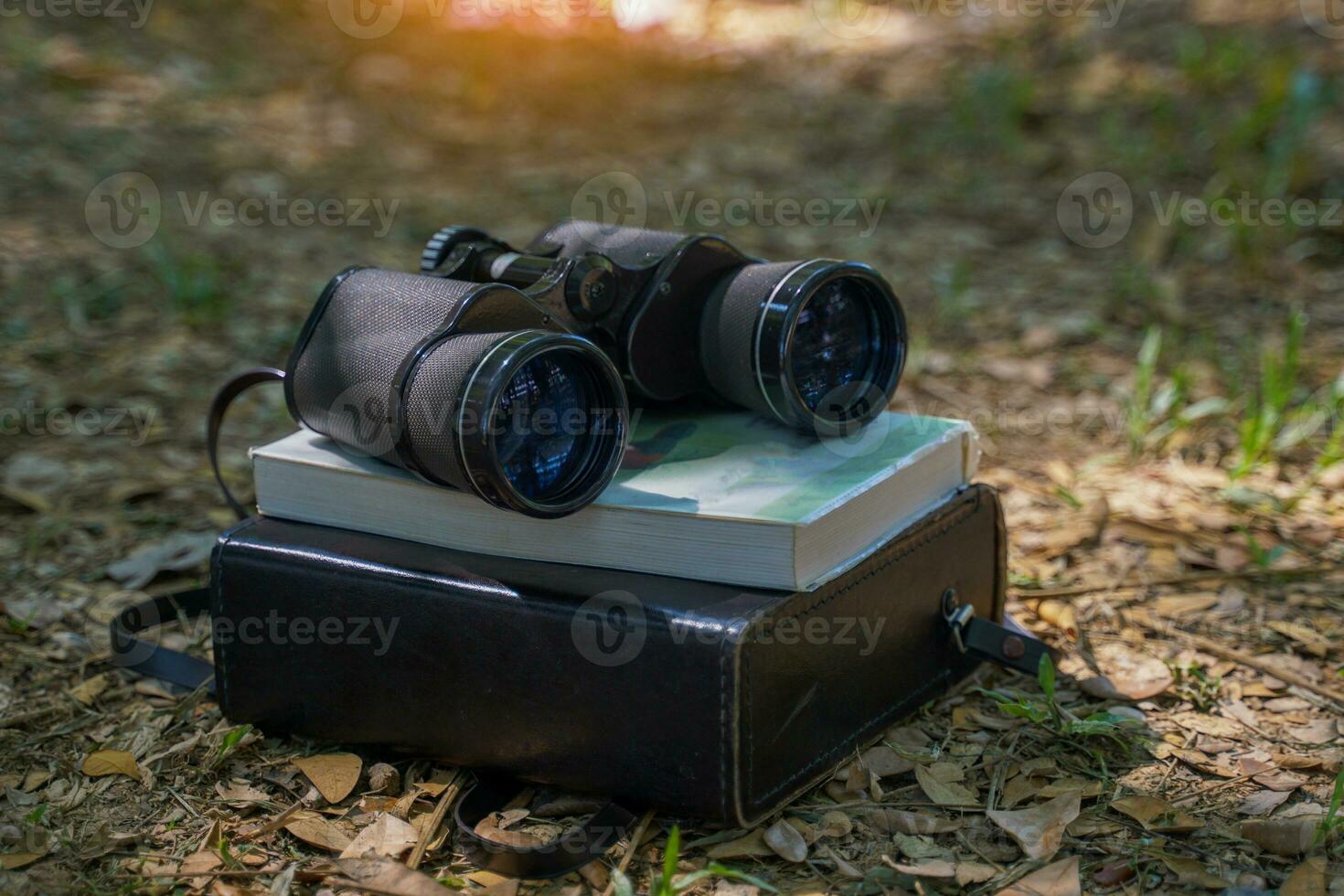 Binoculars, birdwatching guide book and case laying on the ground in the forest It is a device for bird watching, animal viewing, and studying living things in the forest. Soft and selective focus. photo