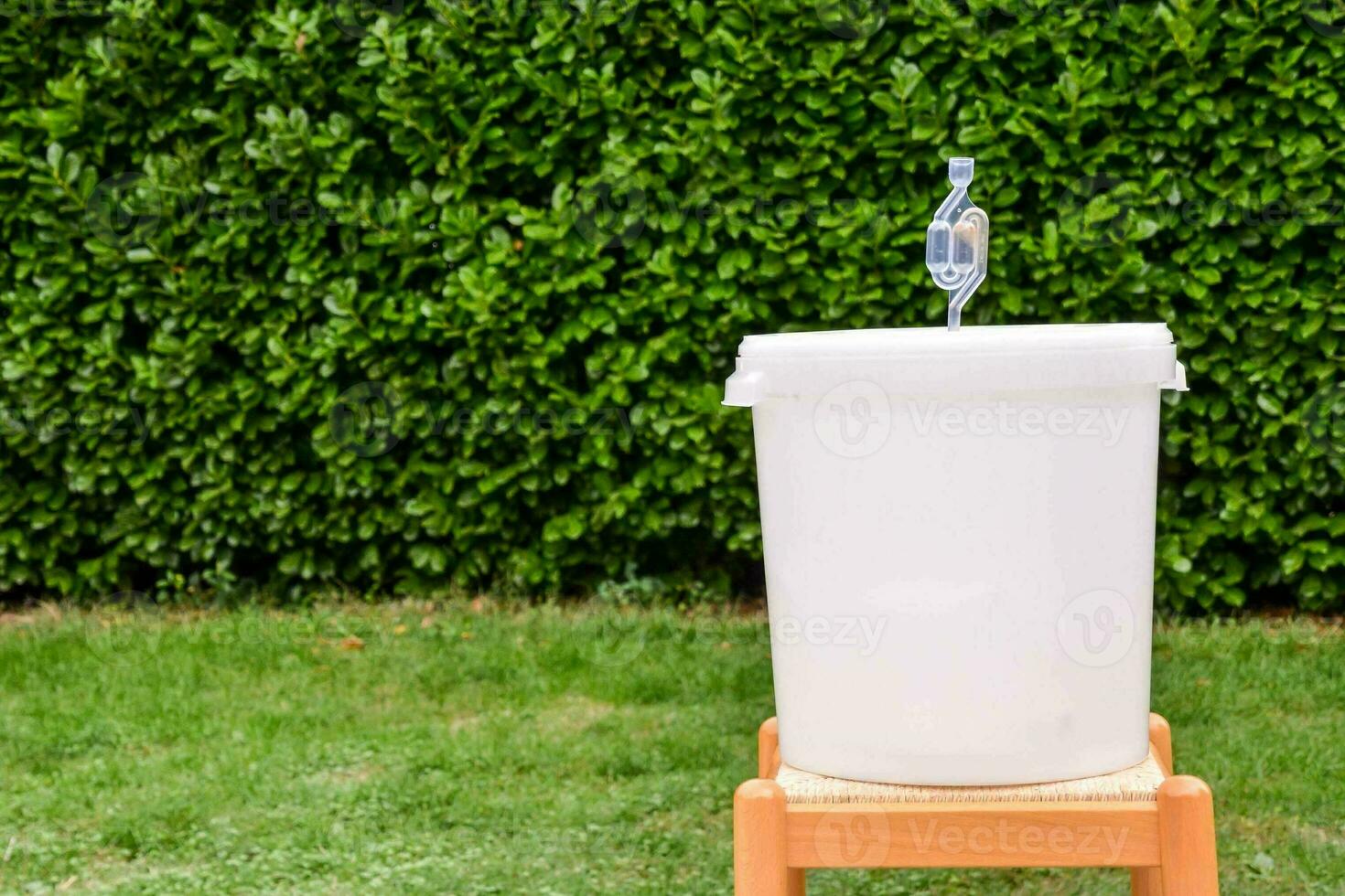 a white bucket sitting on a wooden stool in front of a bush photo