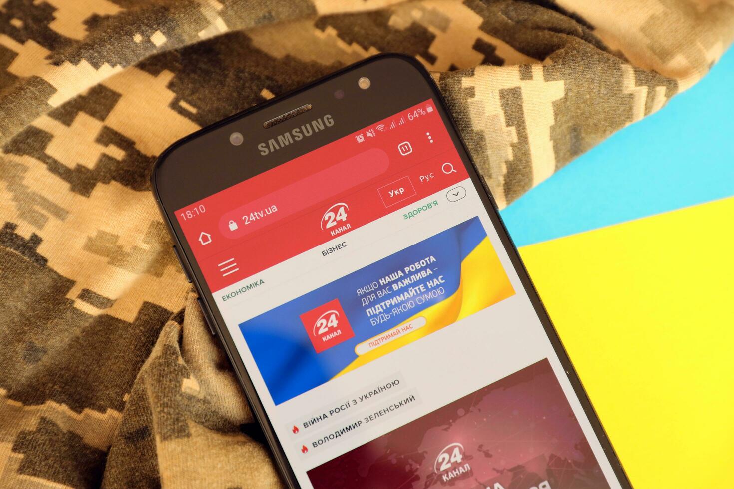 KYIV, UKRAINE - 4 MAY, 2023 24tv ukrainian news portal on smartphone screen with ukrainian flag and camouflage fabric photo