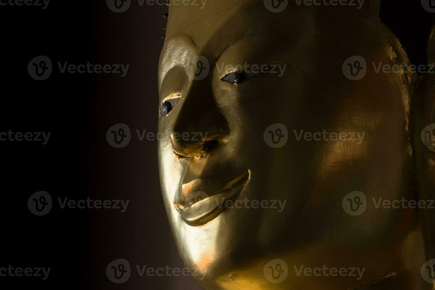 Close up the face of a golden Buddha statue in the dark rooms photo