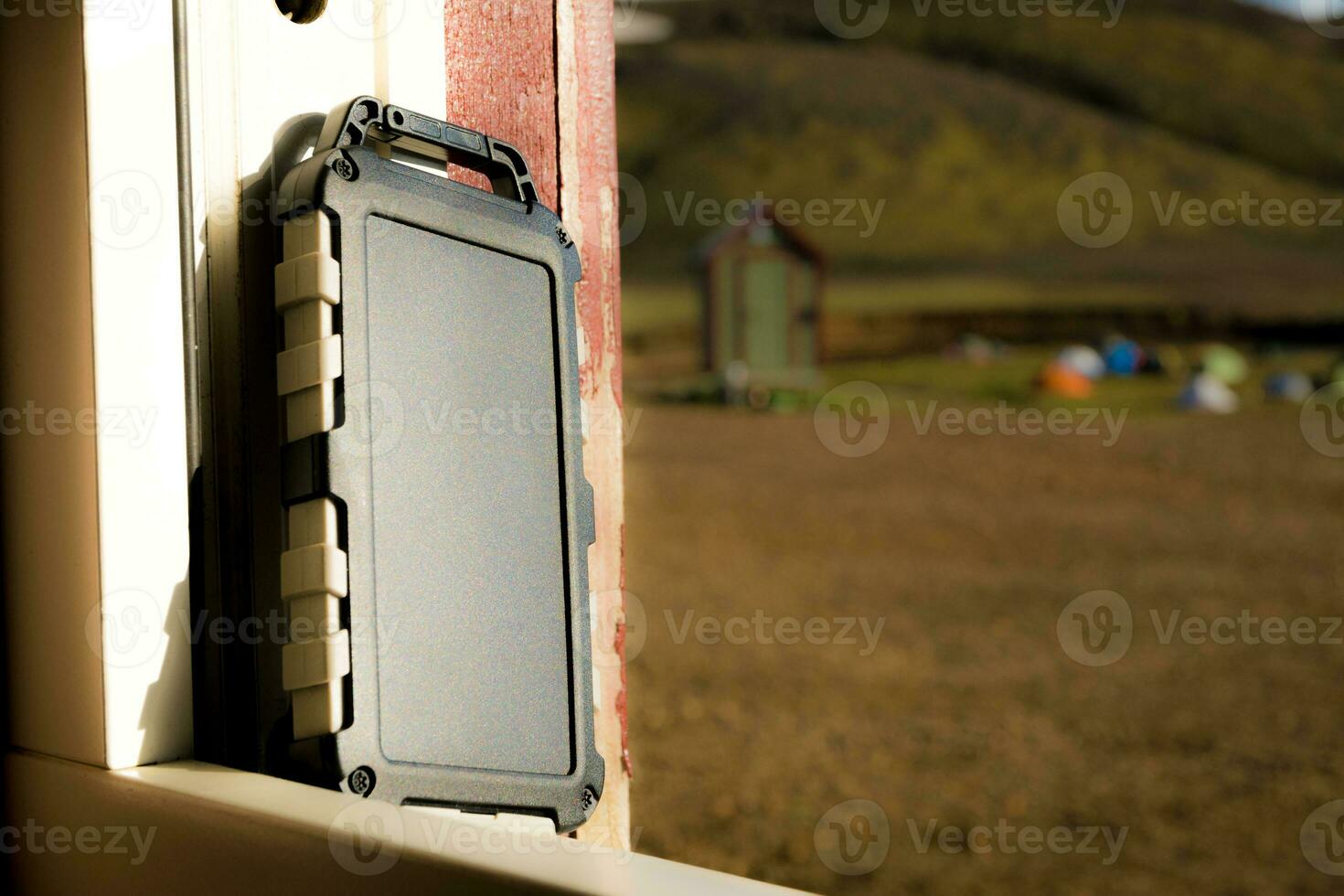 Rugged power bank battery with solar cell charging in the sun, nature and tents of campsite in the background photo