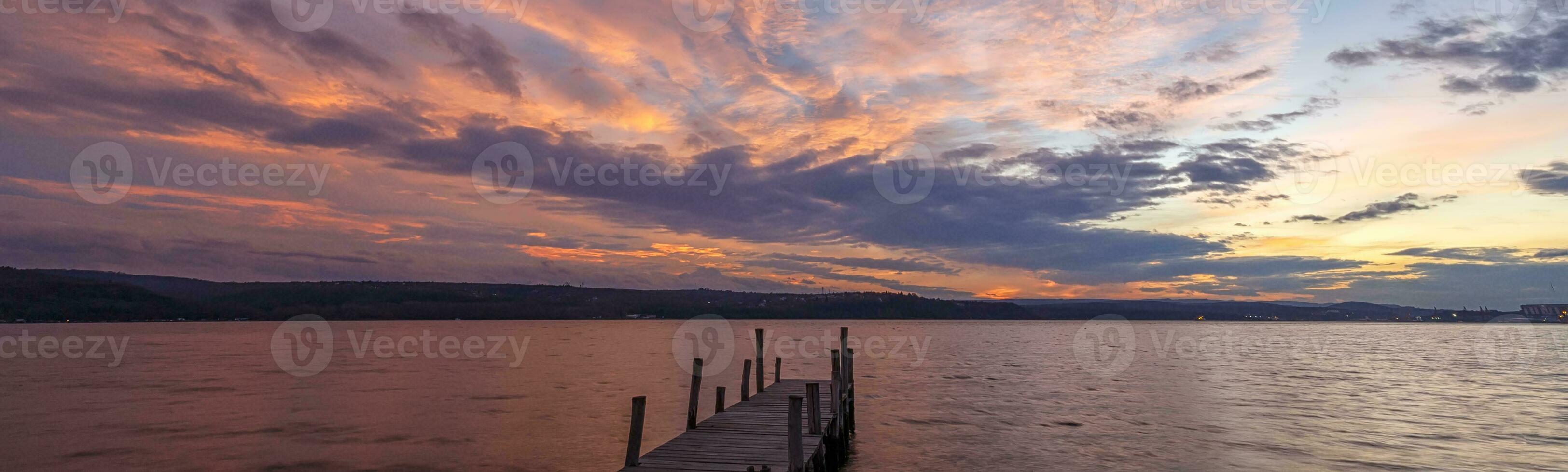 bandera de vistoso puesta de sol a un lago costa a un de madera muelle. foto