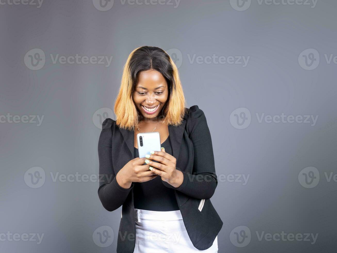 Black lady texting on her phone standing over a gray studio wall background photo