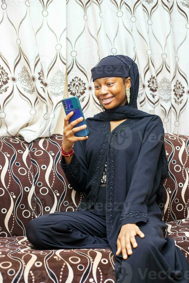 Happy black muslim teen girl holding smart phone app enjoying online virtual chat video call with friends in distance mobile chat virtual meeting, social media at home. photo