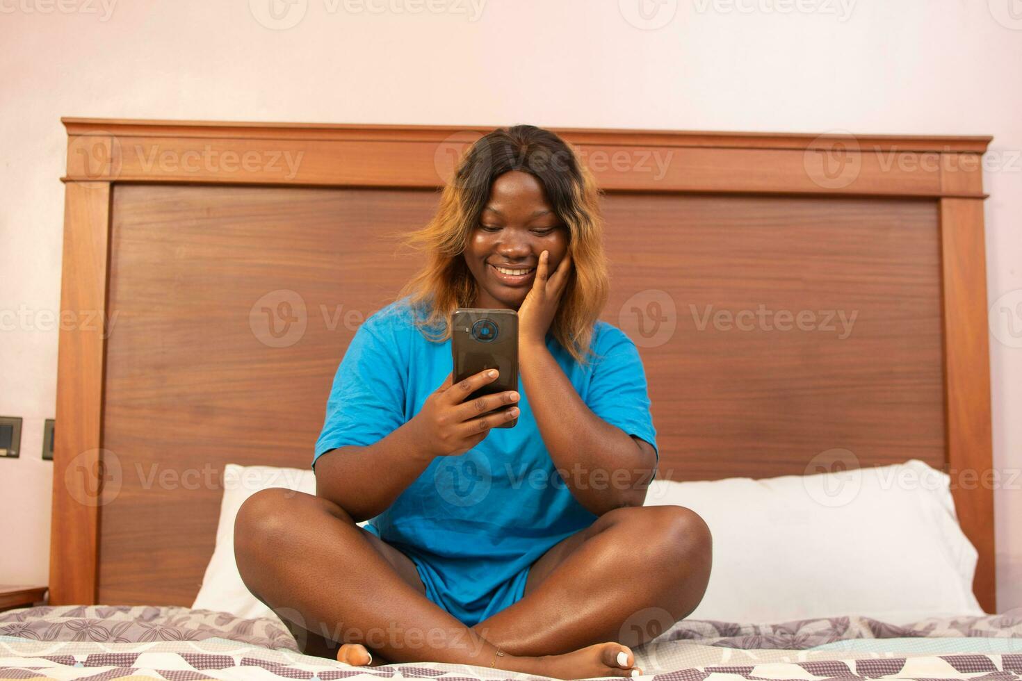 african woman using her phone in bed photo