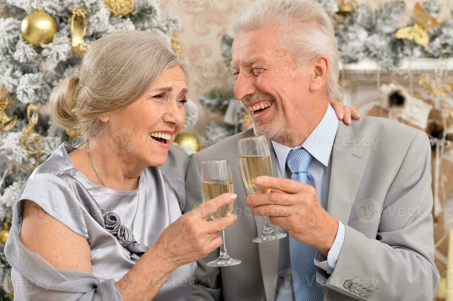 Old couple with champagne celebrating Christmas near tree photo