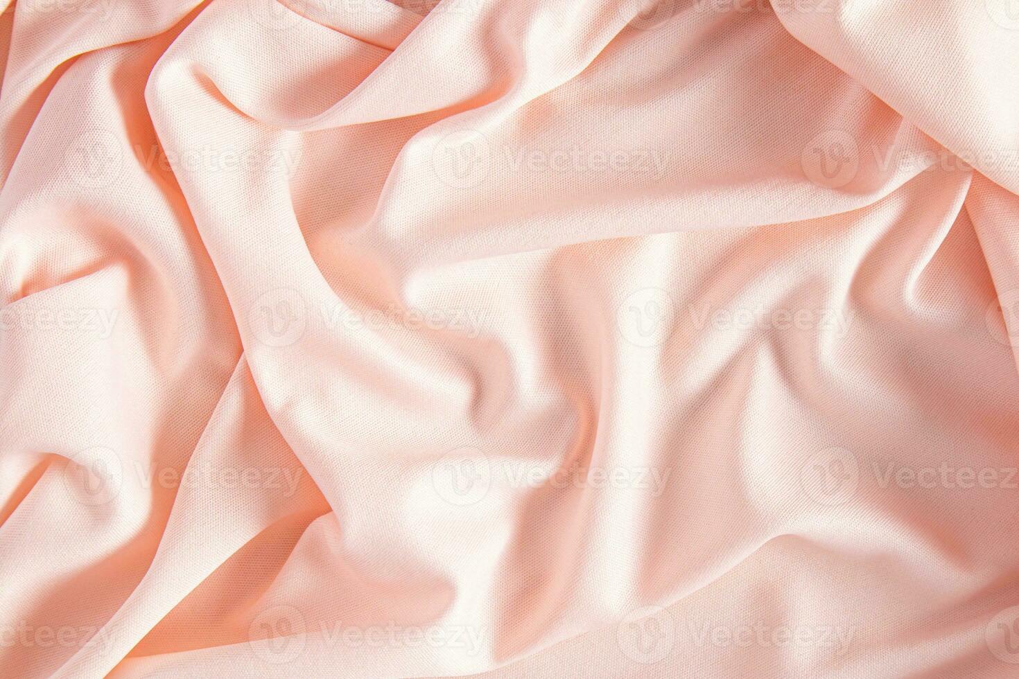 Luxurious satin textiles in peach color. Soft abstract waves of factory fabric. Festive background. Trend Colors of the Year 2024 Peach Fuzz. photo