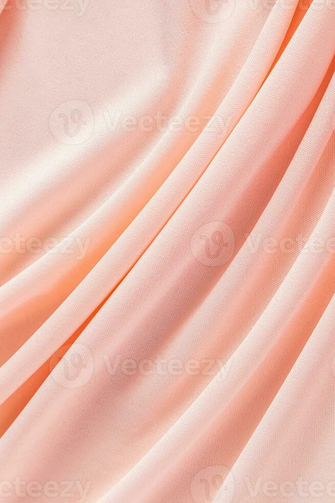 Soft pleats of peach colored satin textiles. Luxury abstract textile background design. Vertical view. Color of the Year 2024 peachy fuzz. photo
