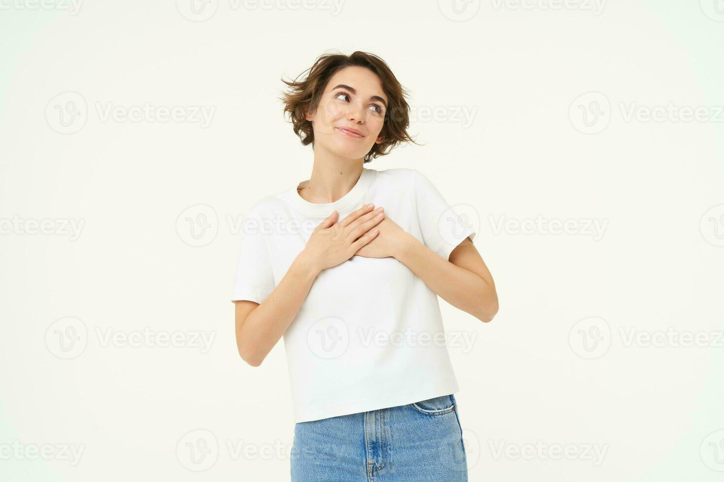 Portrait of woman expressing care, self-love and caring emotions, holds hands on chest, looking with smile at camera, isolated over white background photo