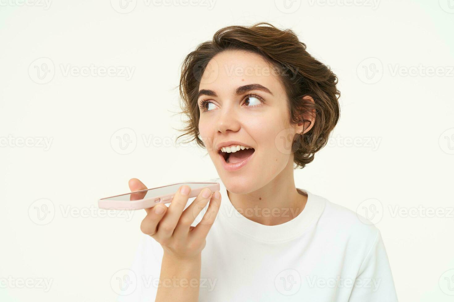 Portrait of woman talking into mobile phone speakerphone, records voice message, translates words, stands over white background photo