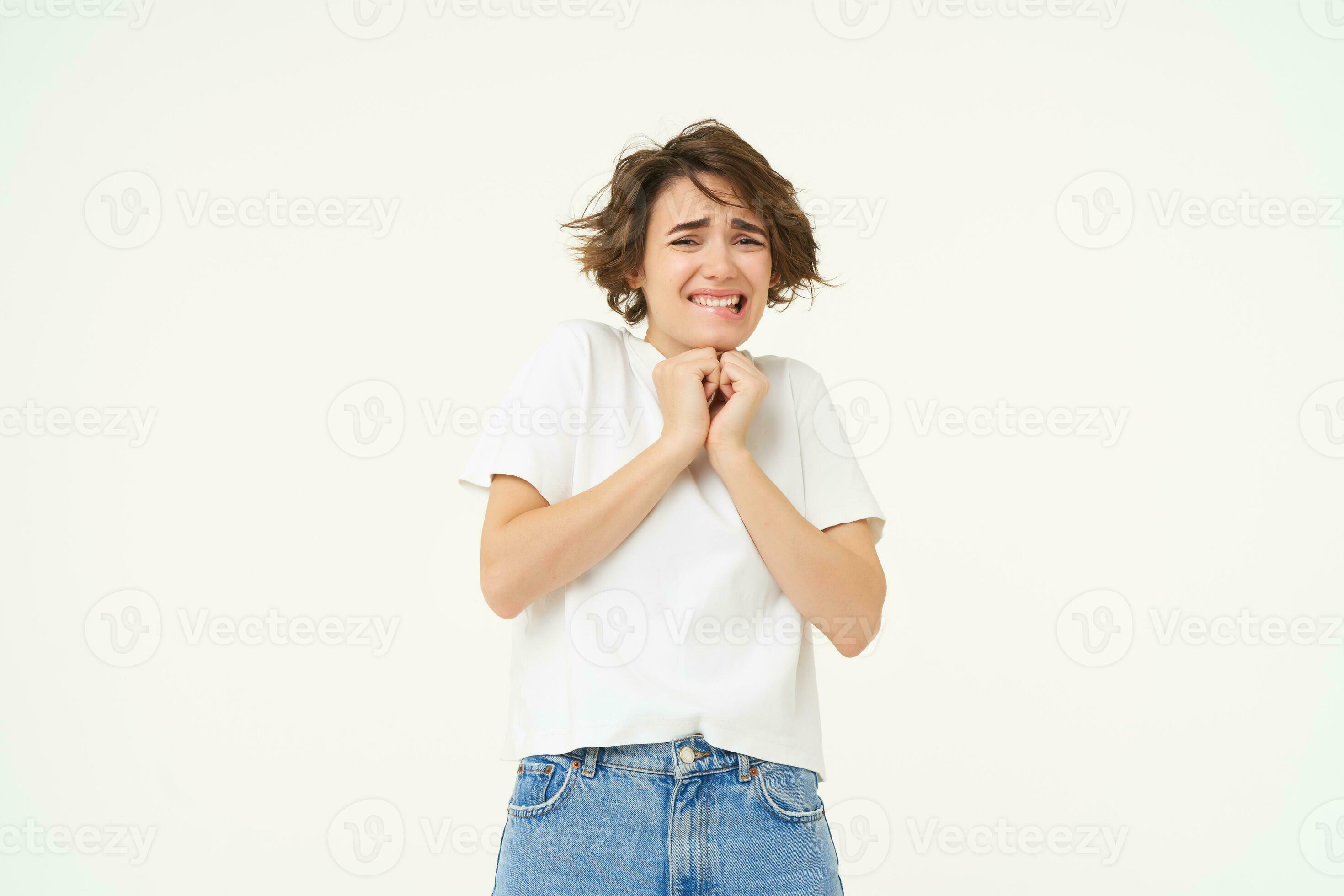 Image of girl jumps from fear, scared, looking frightened, standing against white studio