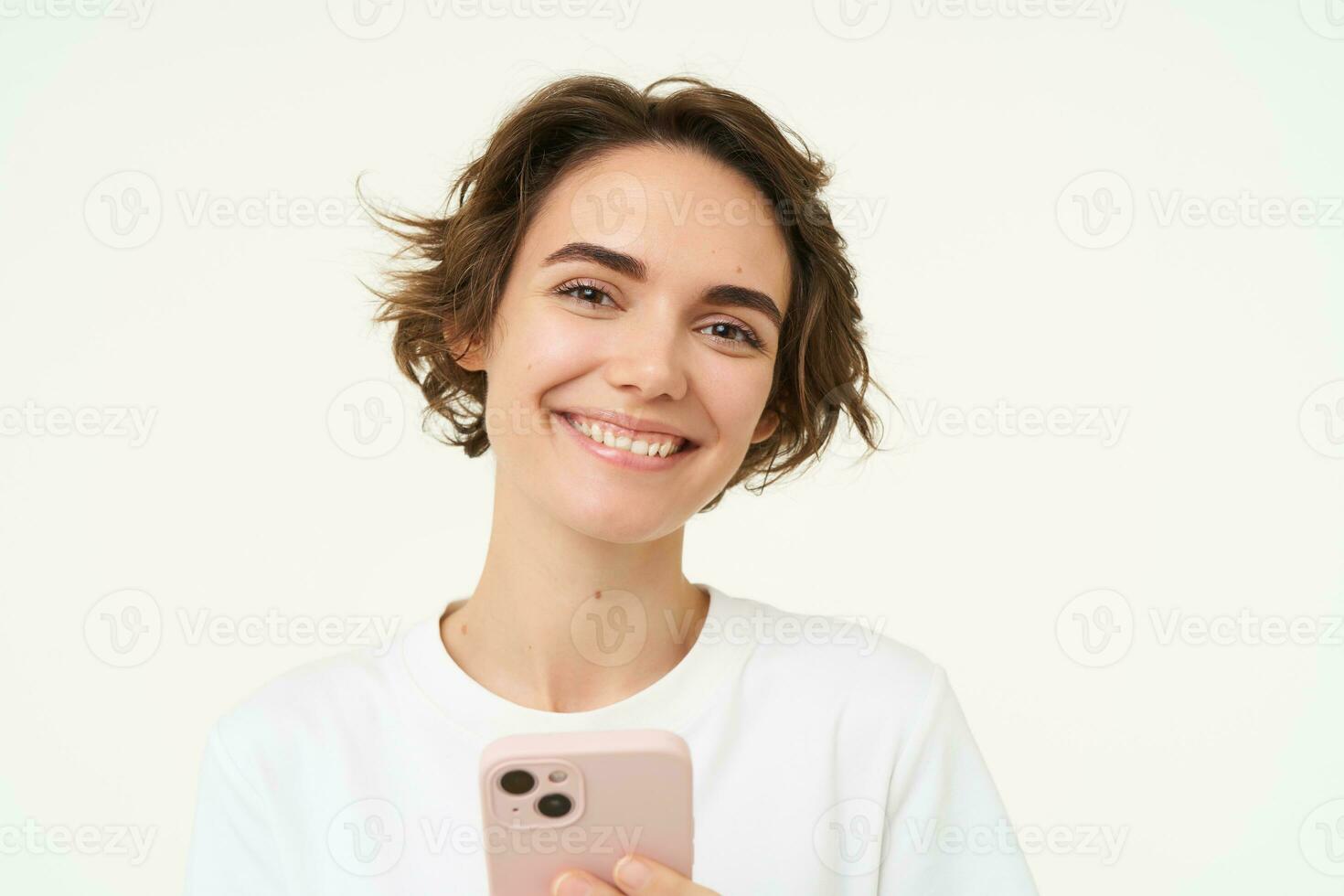 Portrait of young woman standing with pink mobile phone, using smartphone app, doing online shopping, paying for something using application, standing over white background photo