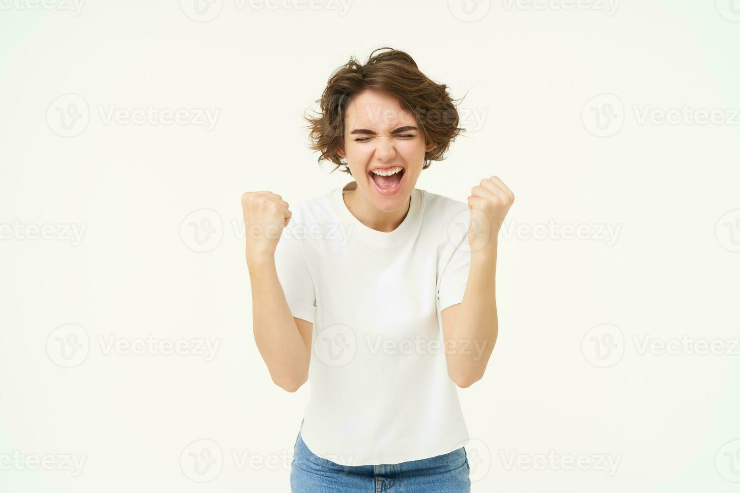 emocionado morena chica, estudiante victorioso premio, celebrando victoria, triunfando, en pie en blanco camiseta y pantalones terminado blanco antecedentes foto