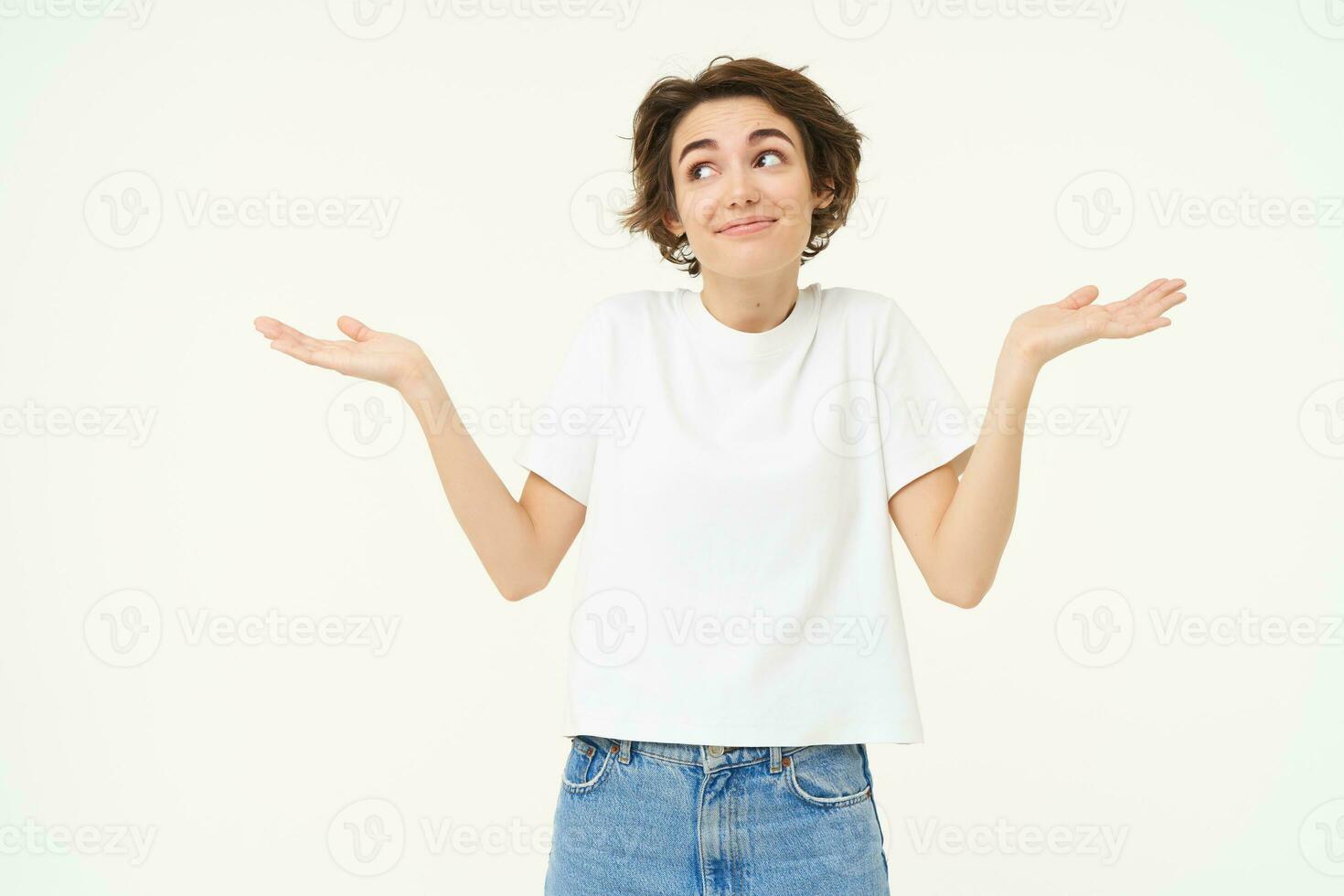 Portrait of girl with short hair, shrugs shoulders, looks unaware, clueless, doesnt know what to do, stands over white studio background photo