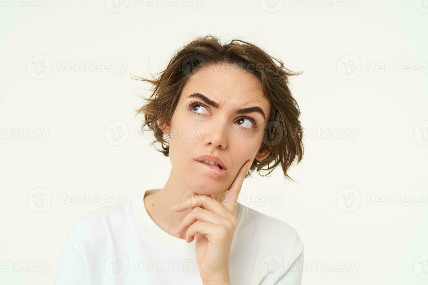Portrait of thinking woman, touches her chin, looks serious and thoughtful, poses over white background photo