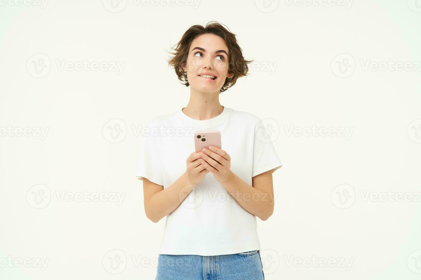 Portrait of brunette girl with smartphone, sending a message, using mobile phone application, smiling and looking happy, white studio background photo