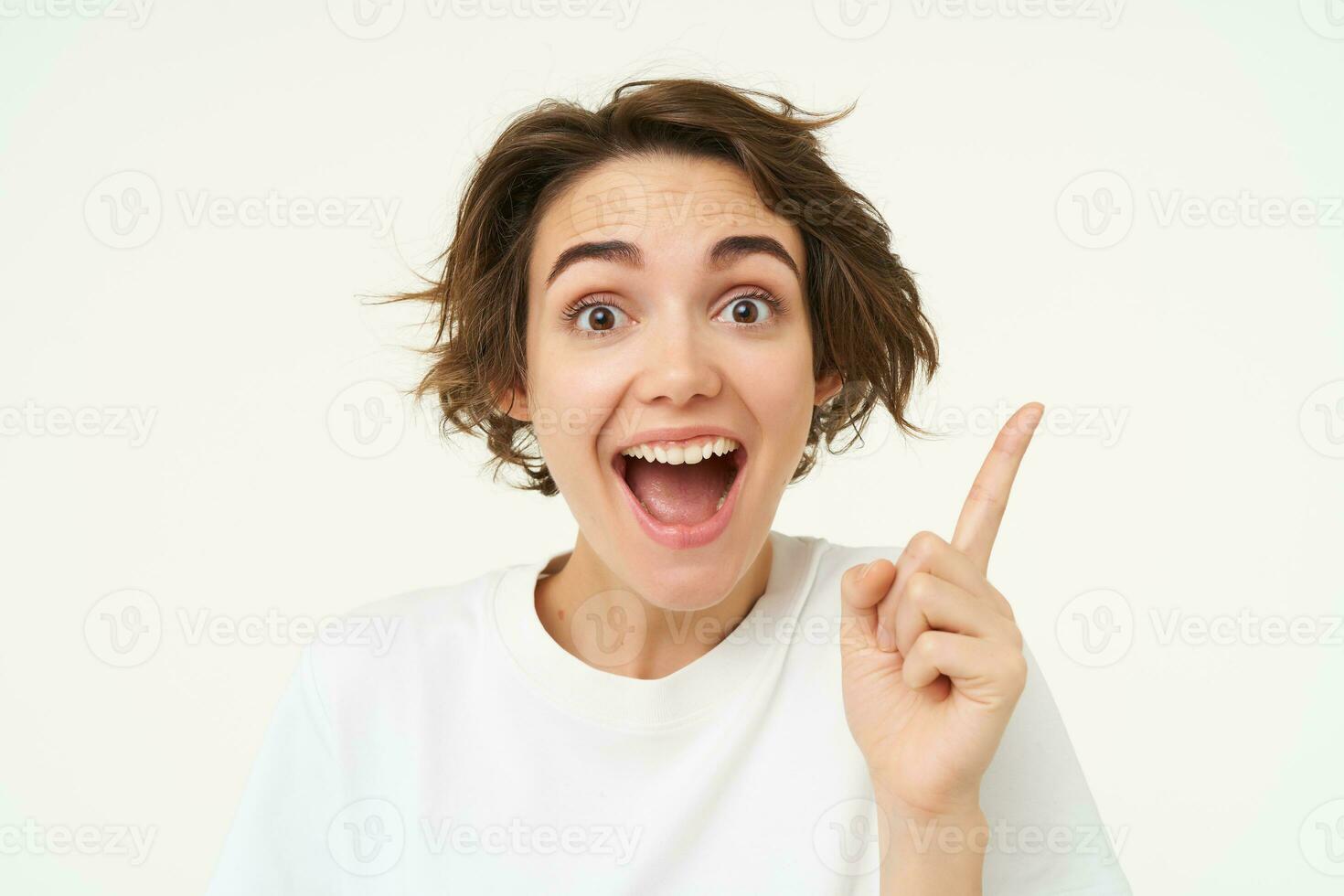 Close up of excited smiling woman, pointing finger up, showing number one, has an idea, thinking of a plan or solution, standing over white background photo