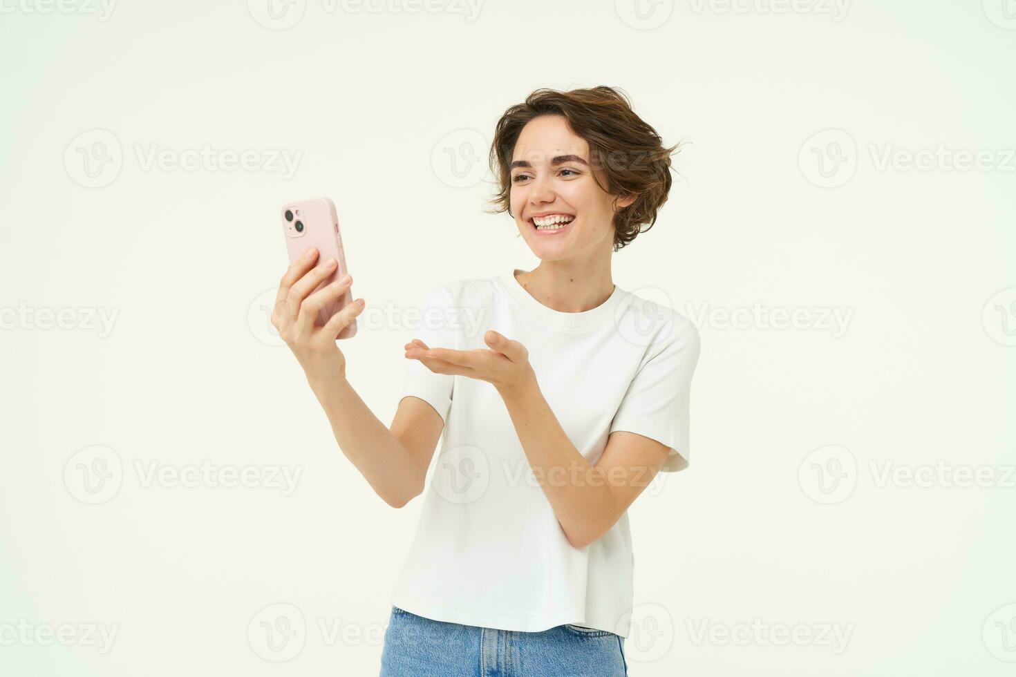 Portrait of girl talking on mobile phone, video chats with friends on smartphone, standing over white studio background photo