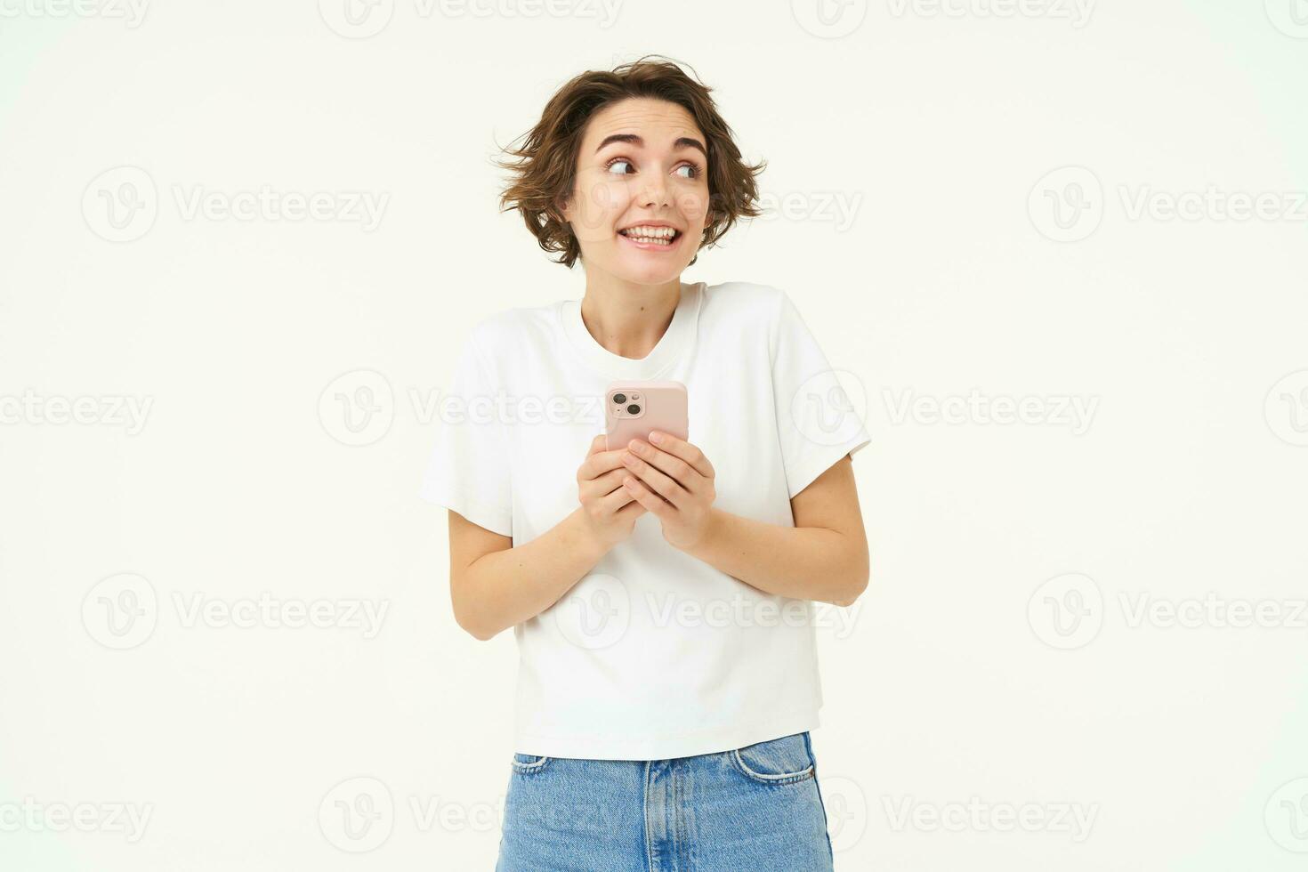 Portrait of brunette girl with smartphone, sending a message, using mobile phone application, smiling and looking happy, white studio background photo
